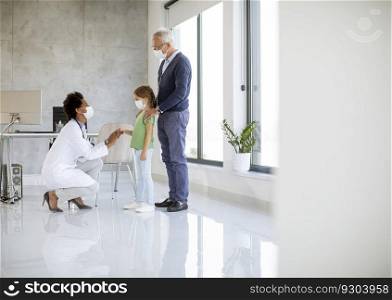 Senior man with his little grandaughter at the pediatrician examination by African american female doctor