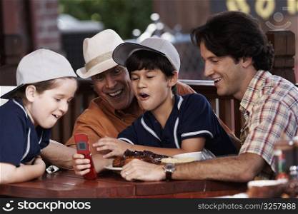 Senior man with his son and two grandchildren looking at a mobile phone