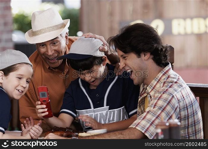 Senior man with his son and two grandchildren looking at a mobile phone and laughing