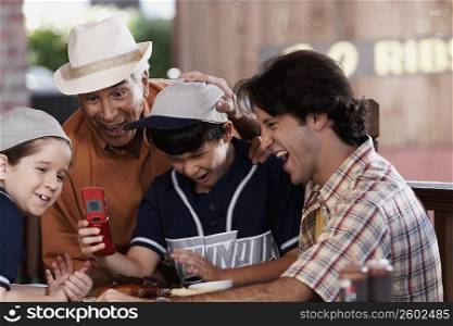 Senior man with his son and two grandchildren looking at a mobile phone and laughing