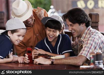 Senior man with his son and two grandchildren looking at a mobile phone and smiling