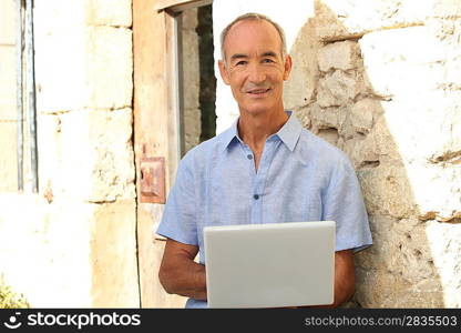 Senior man with laptop in front of stone house