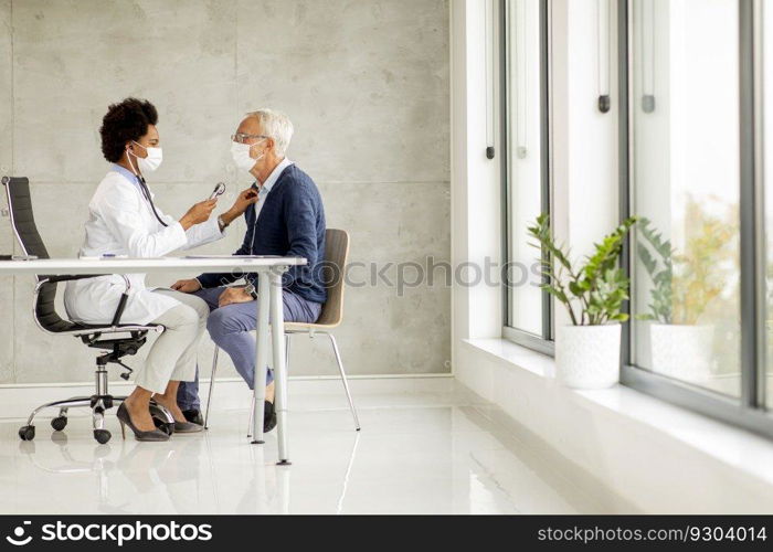 Senior man with protective facial mask receive news from black female doctor in the office