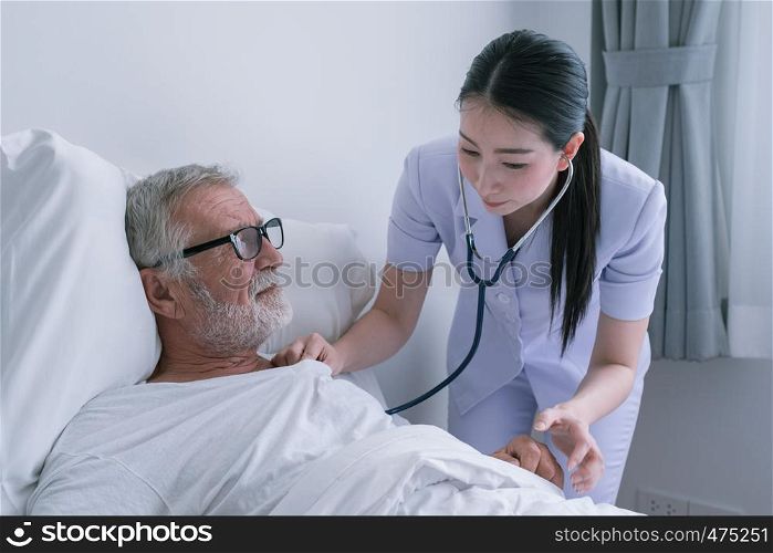 senior man with smiling nurse, takes care and discussion after health check by stethoscope and cheer on bed at nursing home