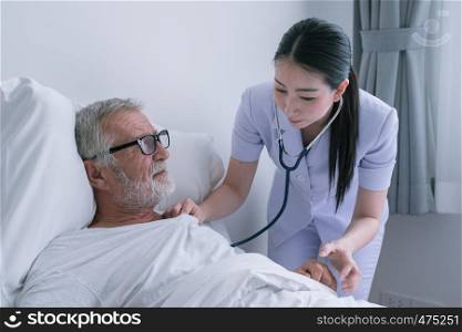 senior man with smiling nurse, takes care and discussion after health check by stethoscope and cheer on bed at nursing home