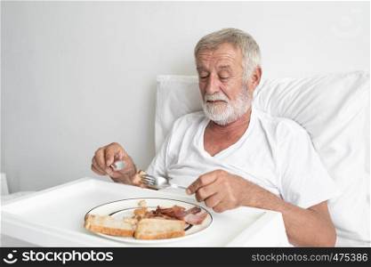 senior man with smiling nurse, takes care breakfast and discussion and cheer on bed at nursing home