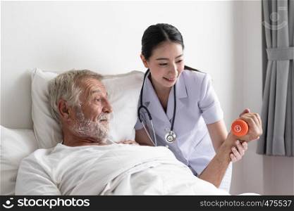 senior man with smiling nurse, takes care health check by weight training and cheer on bed at nursing home