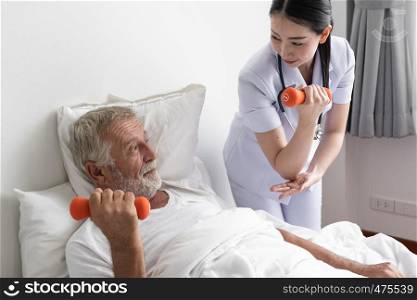 senior man with smiling nurse, takes care health check by weight training and cheer on bed at nursing home