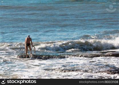 Senior man with swim cap prepares to swim in rough sea, waves