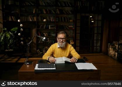 Senior man working with documents at home office. Elderly male sitting at table in library looking at camera. Senior man working with documents at home office