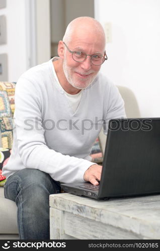 Senior man working with laptop sitting in sofa