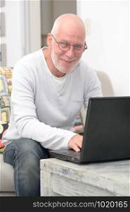 Senior man working with laptop sitting in sofa