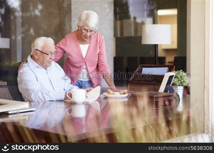 Senior Man Writing Memoirs In Book Sitting At Desk