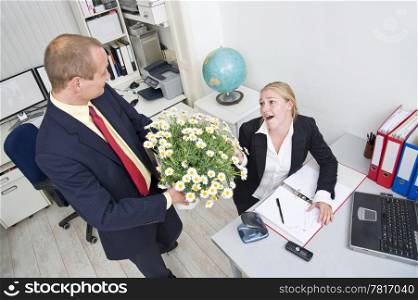Senior manager giving his younger female associate a large flower pot with white daisies