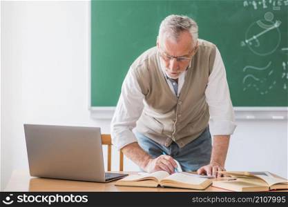 senior math teacher writing with pen while standing against chalkboard