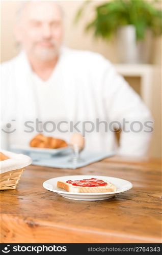 Senior mature man - breakfast at home, focus on bread with marmalade