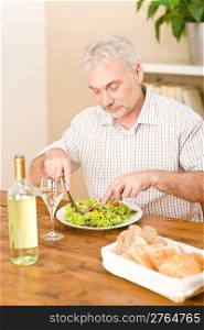 Senior mature man eat vegetable salad and white wine at wooden table, focus on salad