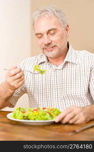 Senior mature man eat vegetable salad at wooden table