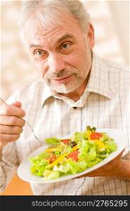 Senior mature man eat vegetable salad at wooden table