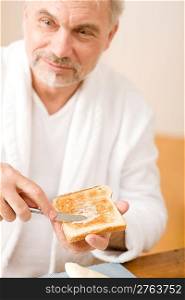 Senior mature man having breakfast butter toast wear bathrobe