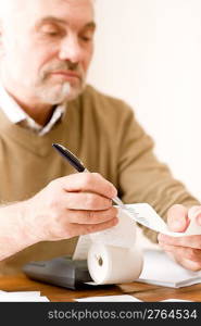 Senior mature man - home office using paper tape calculator