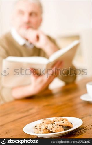 Senior mature man reading book, cookies at wooden table