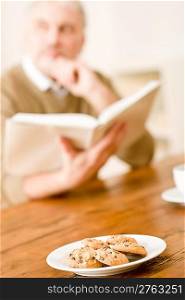 Senior mature man reading book, cookies at wooden table