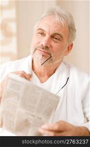 Senior mature man thoughtful read newspaper holding glasses
