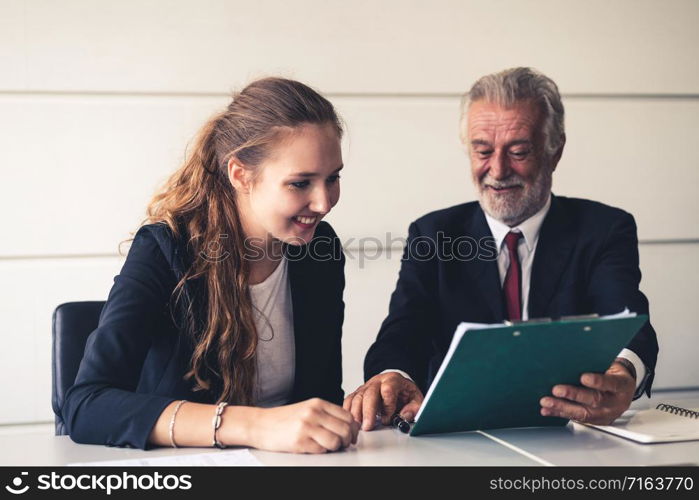 Senior old executive manager working with young businesspeople in office meeting room. Old man is the company leader sitting with secretary looking at financial report.