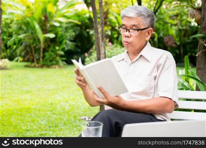 senior old man reading a book in the park and drinking water. Concept of retirement lifestyle and hobby.