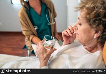 Senior patient taking a pill next to his female doctor. Senior patient taking a pill