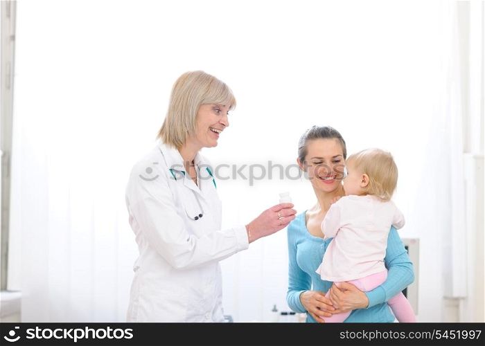 Senior pediatric doctor giving pills bottle to mother with baby