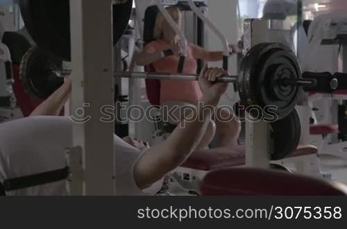 Senior people having workout in the gym. Man lifting bar-bell and woman exercising on chest press machine