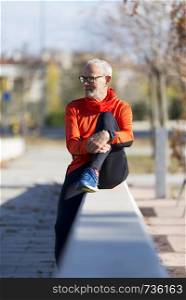 Senior runner man sitting after jogging in a park