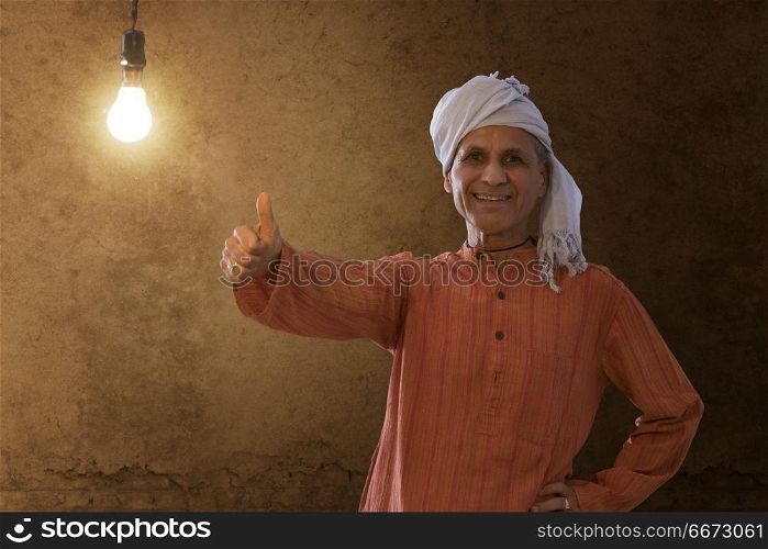 Senior rural man showing thumb up while standing against light bulb