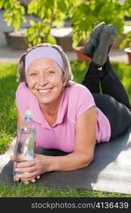 Senior sportive woman lying on mat drink water outside sunny day