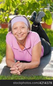 Senior sportive woman on mat listen music outside sunny day