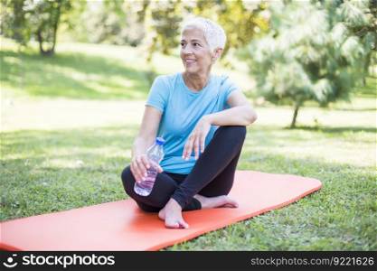 Senior sportive woman sitting on mat outside and resting after workout