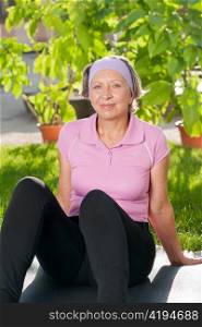 Senior sportive woman sitting on mat outside sunny day