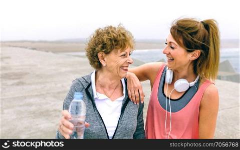 Senior sportswoman laughing with female friend by sea pier. Senior sportswoman laughing with female friend