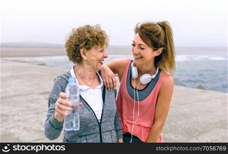 Senior sportswoman laughing with female friend by sea pier. Senior sportswoman laughing with female friend
