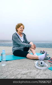 Senior sportswoman relaxing on yoga mat by sea pier. Senior sportswoman relaxing on yoga mat