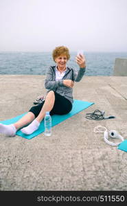 Senior sportswoman taking selfie by sea pier. Senior sportswoman taking selfie