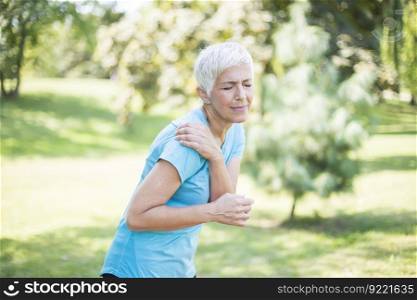 Senior sporty woman having shoulder pain in the park