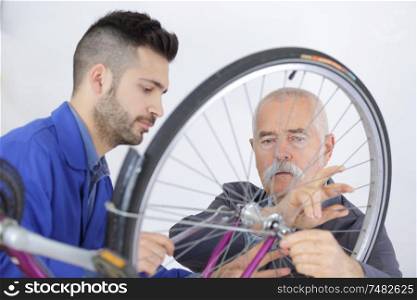 senior talking to apprentice while fixing bike wheel