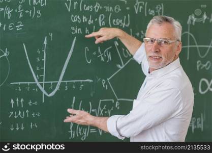 senior teacher glasses explaining math example green chalkboard