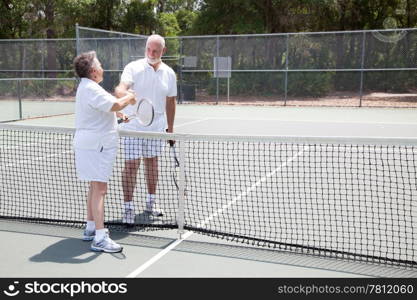 Senior tennis players shake hands over the net. Wide shot with room for text.