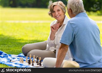 Senior wife and husband playing chess on blanket summer park