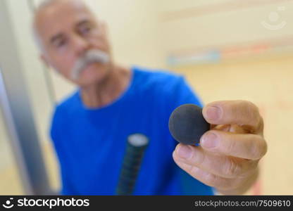 senior with a racket holding a tennis ball