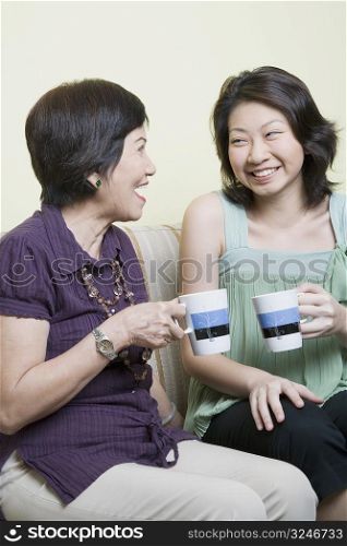 Senior woman and her granddaughter holding cups and smiling